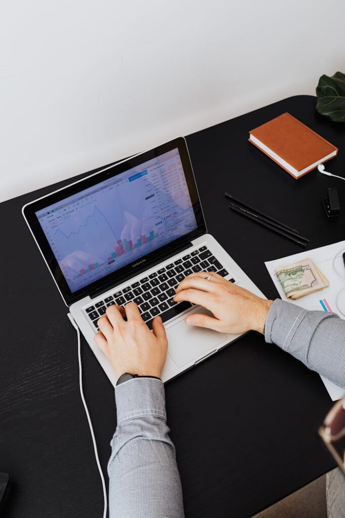Hands typing on a laptop showing graphs on screen, analyzing financial data.